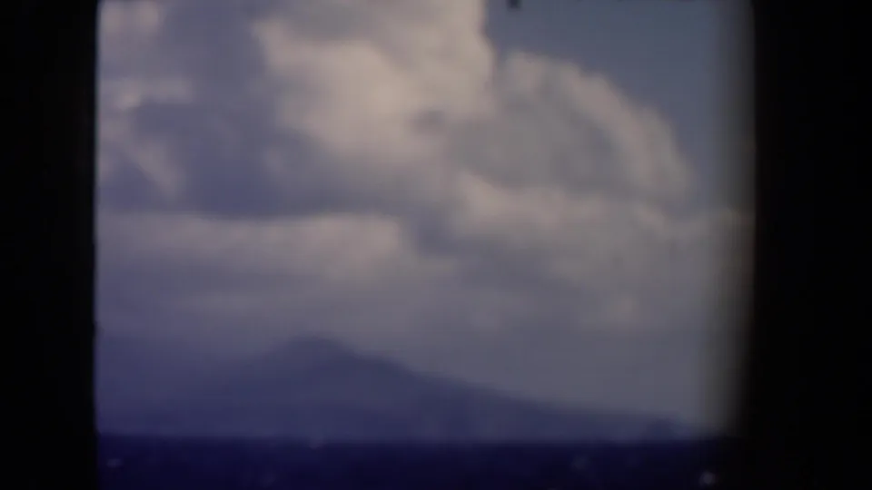 1946 8mm home-movie frame from the Netherlands showing clouds, blue sky, and a distant hazy hill or mountain through dark window framing.