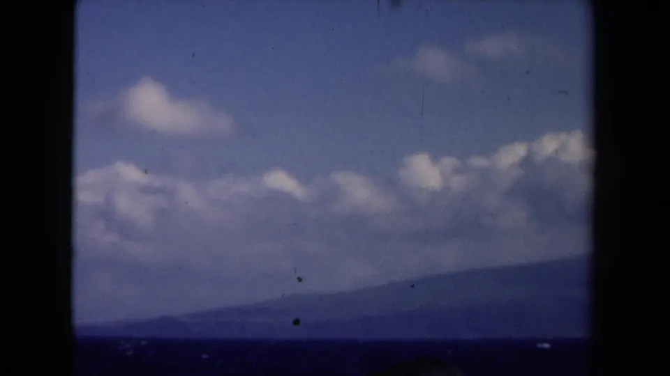 1946 Netherlands 8mm home-movie frame of clouds, blue sky, and a hazy distant landform viewed through dark window-like framing.