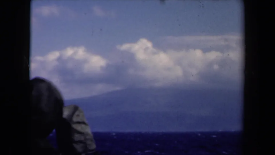 1946 Netherlands 8mm frame with a partial silhouetted passenger at lower left and a soft view of ocean, distant land, and clouds.