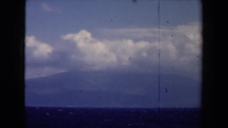 1946 8mm Netherlands seascape frame showing open water, a distant mountainous coastline, cloud-filled sky, grain, and vertical film scratch.