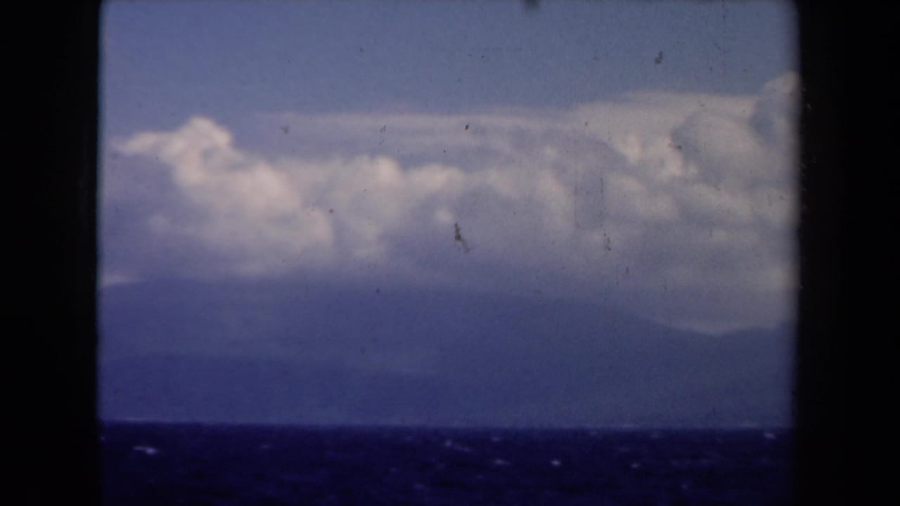 1946 Netherlands 8mm view of dark sea, hazy mountain landforms, and low clouds seen from a boat.