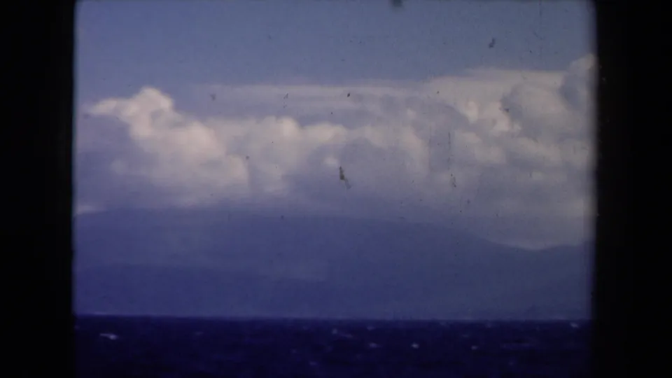 1946 Netherlands 8mm view of dark sea, hazy mountain landforms, and low clouds seen from a boat.