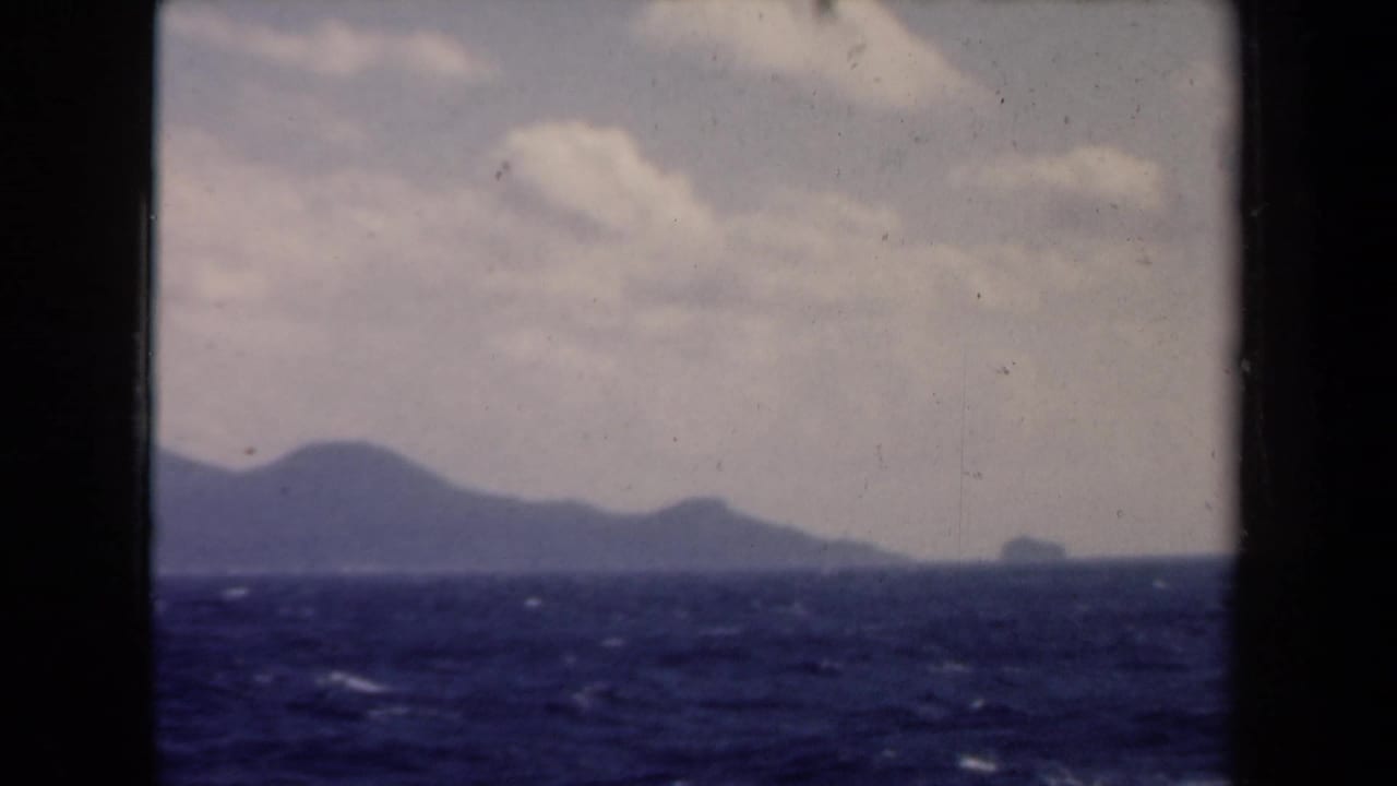 Cloudy sky over choppy sea with distant mountainous land on the horizon.