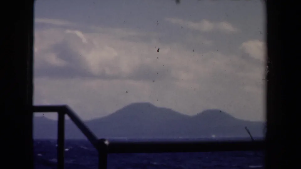 1946 Netherlands 8mm boat perspective with railing in the foreground and hazy mountains across the sea.