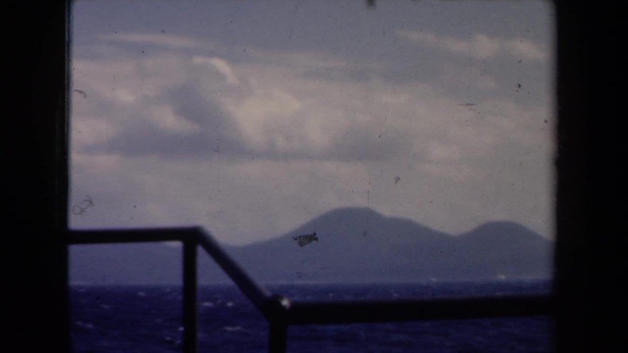 Boat-window view over dark choppy water toward distant land beneath a cloudy sky.