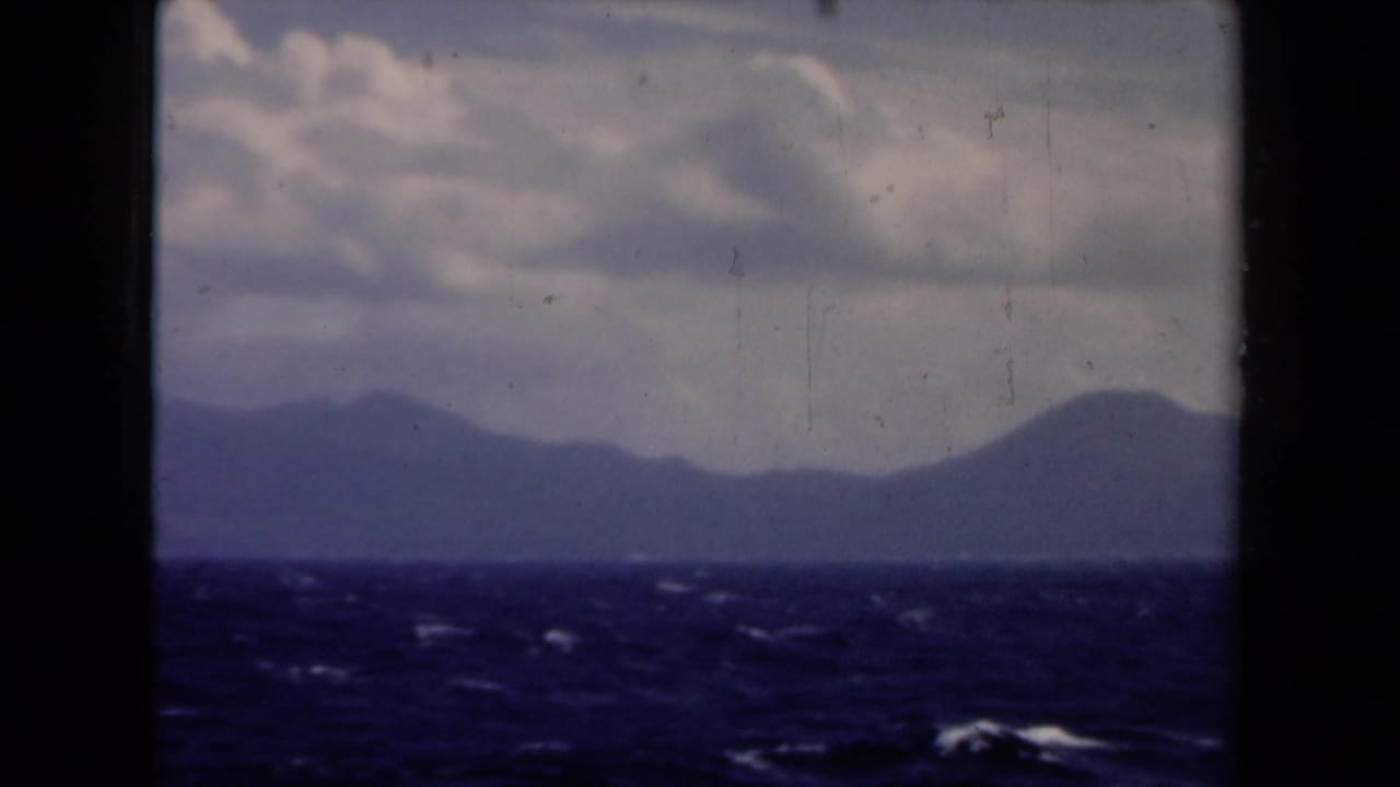 Open water and distant land seen through a dark vertical boat-window frame.