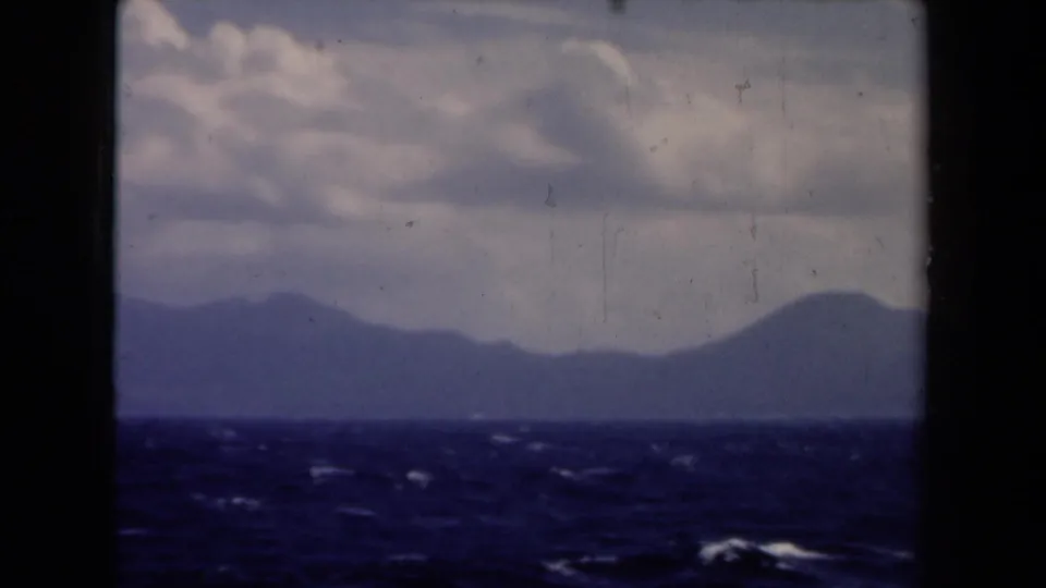 1946 Netherlands 8mm frame with blue water, distant horizon land, clouds, and dark boat-window framing.