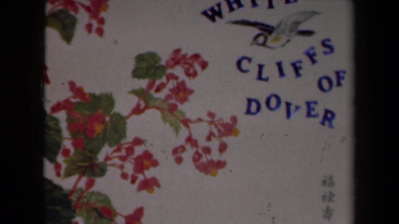 1946 Netherlands 8mm frame showing a filmed decorative White Cliffs of Dover card with blue text, a bird, pink flowers, and green leaves.
