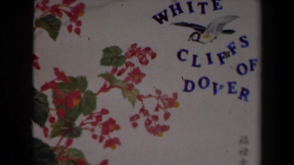 1946 Netherlands 8mm frame showing a filmed White Cliffs of Dover title card with floral artwork and small corner characters near the lower right.