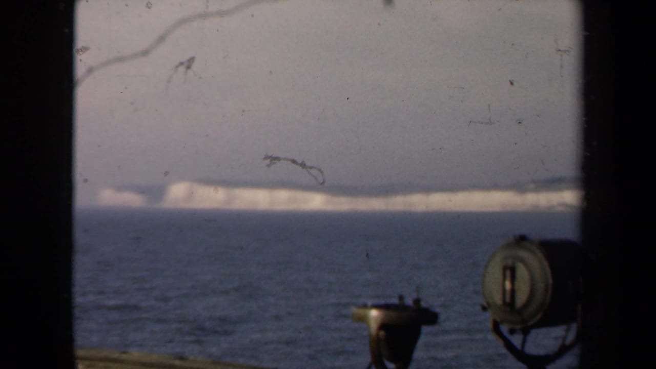 Distant White Cliffs of Dover seen from a ship at sea, with deck equipment and window framing in the foreground.