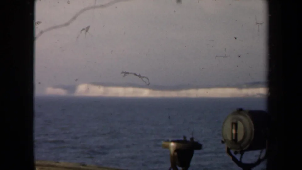 Distant White Cliffs of Dover seen from a ship at sea, with deck equipment and window framing in the foreground.