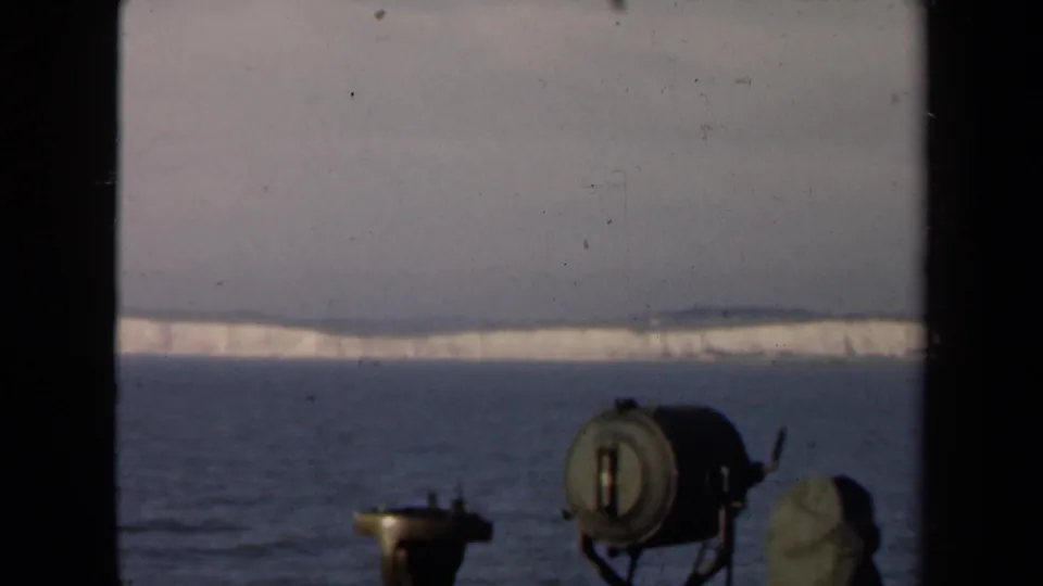 Distant White Cliffs of Dover across open water, framed by shipboard equipment and soft 8mm film grain.