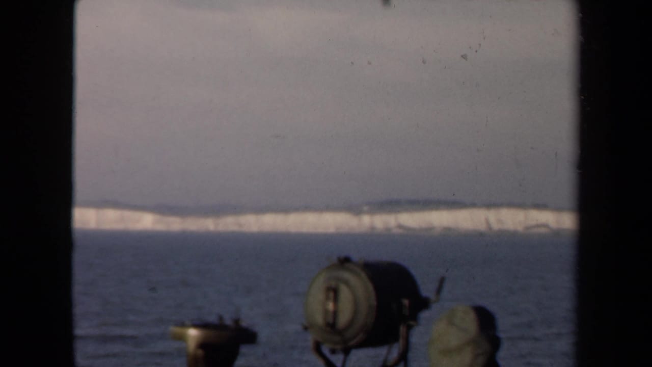 Calm water and a pale snowy shoreline seen past dark film-frame edges and foreground equipment.