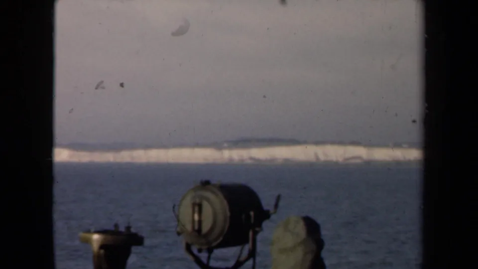 A 1940s Netherlands home-movie frame looking across water to snow-bright land, partly blocked by foreground equipment and dark borders.
