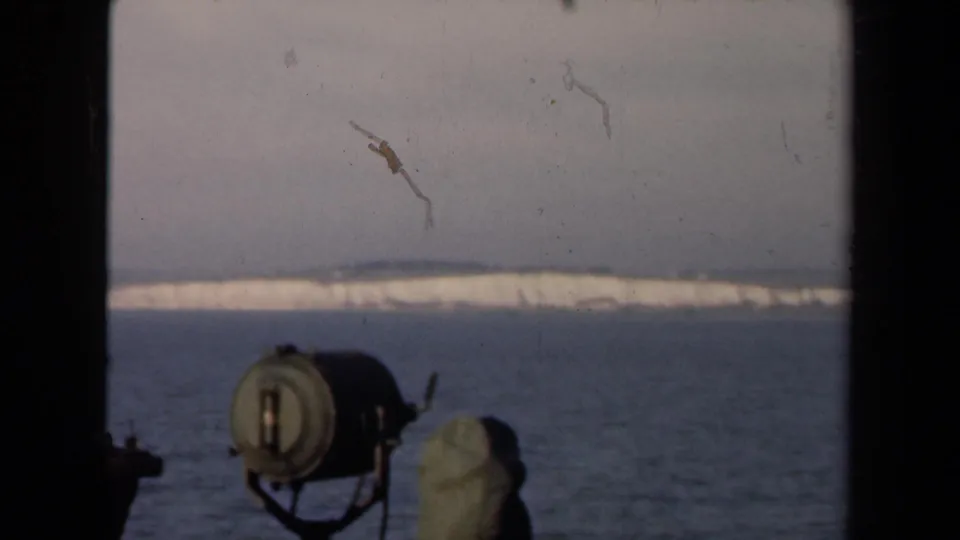 Netherlands 1946 8mm frame with calm water, a pale snow-covered shore, visible film scratches, and boat-like gear at the lower edge.