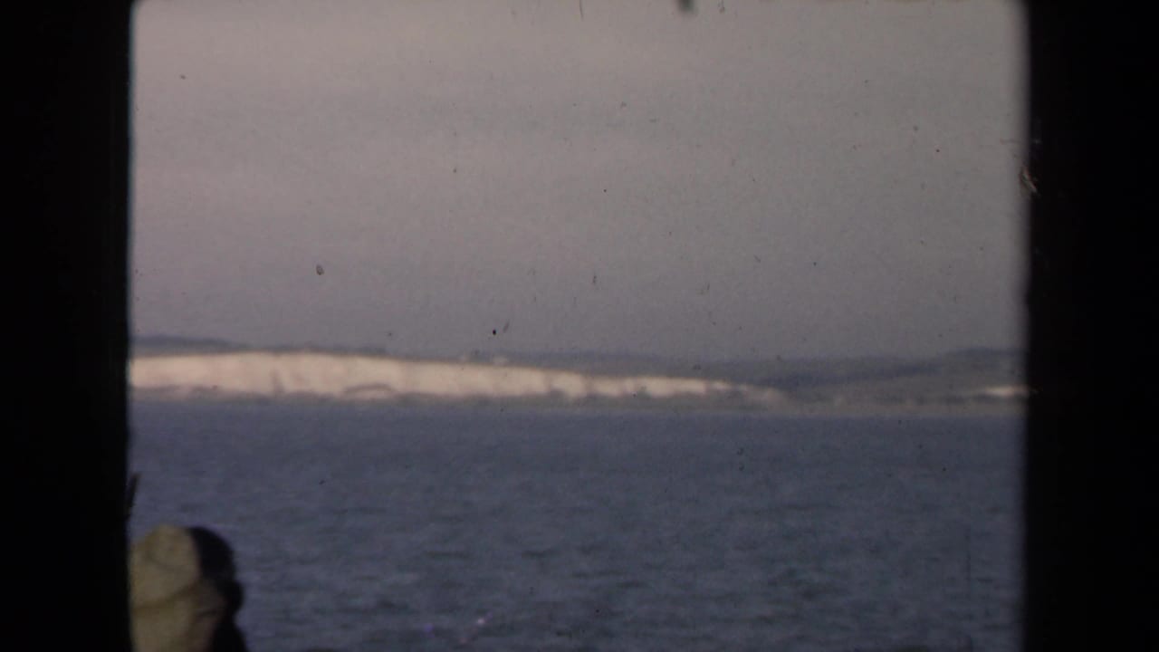 Pale coastal cliffs and dark window bars above a calm sea.