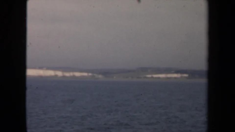 The final frame holds on a distant pale coastline and low hills across blue-gray water, bordered by dark ship-window framing.