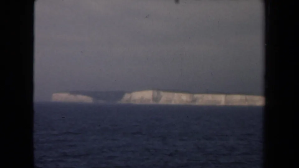 1946 Netherlands 8mm frame showing distant white cliffs across a restless dark sea beneath an overcast sky.