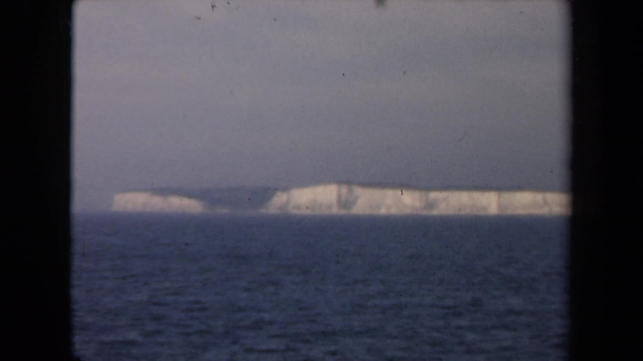 Distant chalk cliffs and dark sea seen through a vertical black frame edge.
