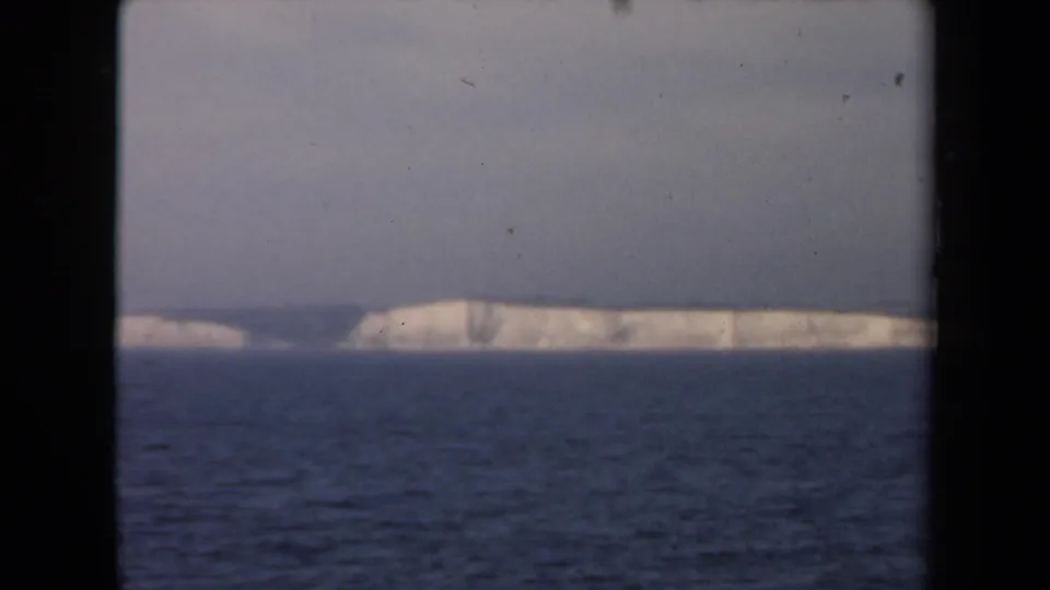 1946 Netherlands 8mm frame of a long pale cliff line above restless dark sea, with muted color and grain.