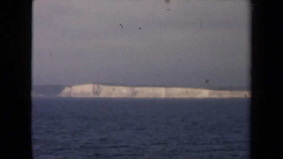 1946 Netherlands home-movie frame showing pale coastal cliffs over dark water, bordered by the scanned film frame.
