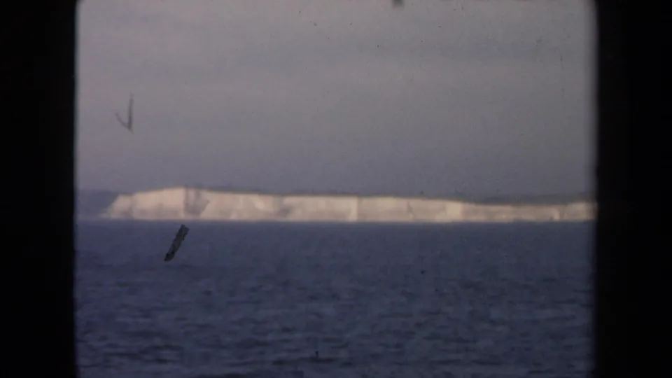 1946 8mm frame showing a distant white iceberg or ice-covered shoreline beyond dark blue water, with heavy black borders and visible film dust.