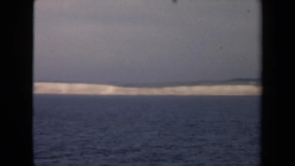 Faded 1946 8mm frame with a low white ice line or distant iceberg across the horizon and dark ocean filling the foreground.