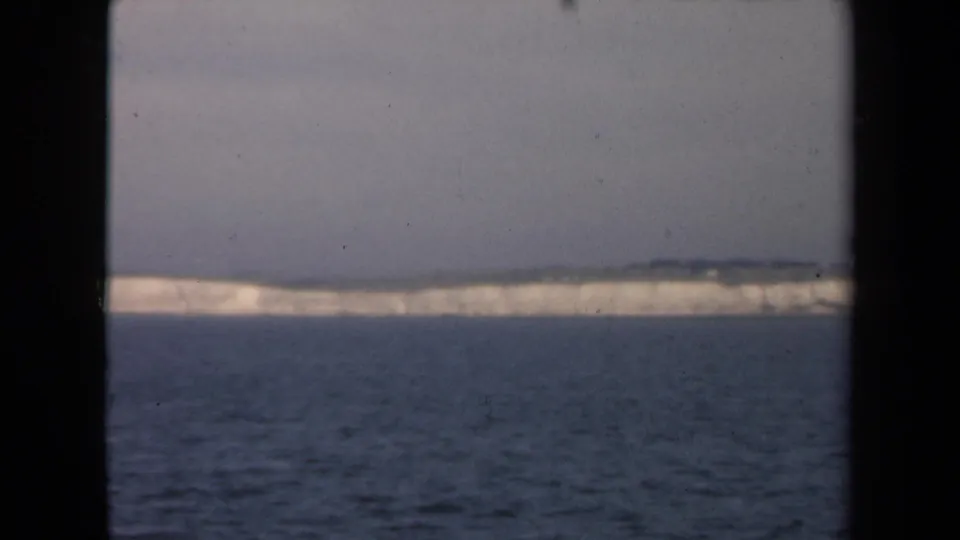 Final 8mm frame showing a distant pale iceberg or ice-covered coast across the water, bordered by dark film edges and light archival wear.