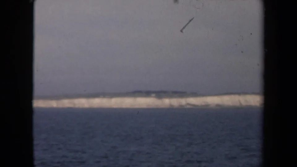 Distant white ice or cliff-like coastline across open water, framed by the dark edges of an 8mm film scan.