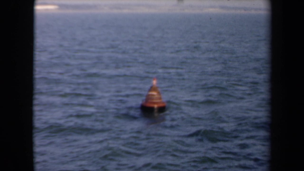 The 1946 Netherlands coastal shot settles on an orange floating buoy, with choppy water and a pale shoreline behind it.