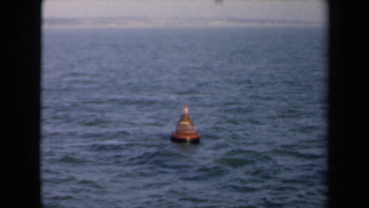 1946 Netherlands 8mm frame showing a small orange conical buoy on open water, seen through dark film-gate edges.