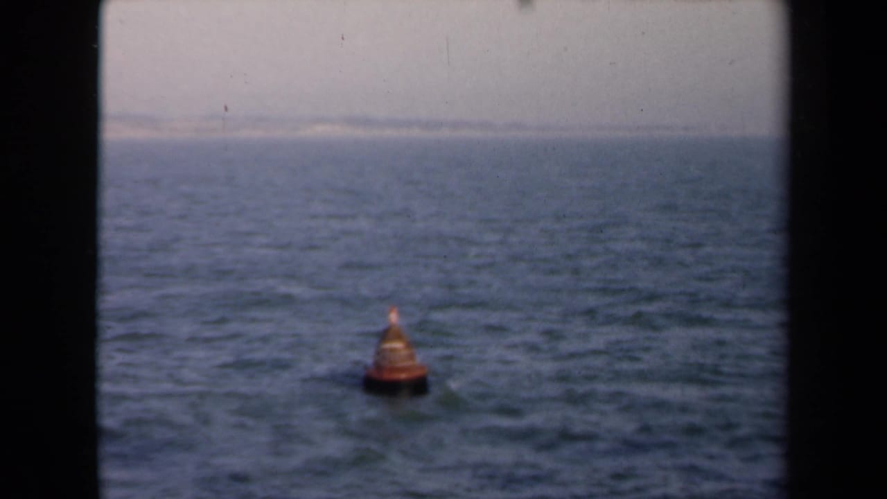 Small orange buoy farther across choppy water with horizon and pale sky behind it.