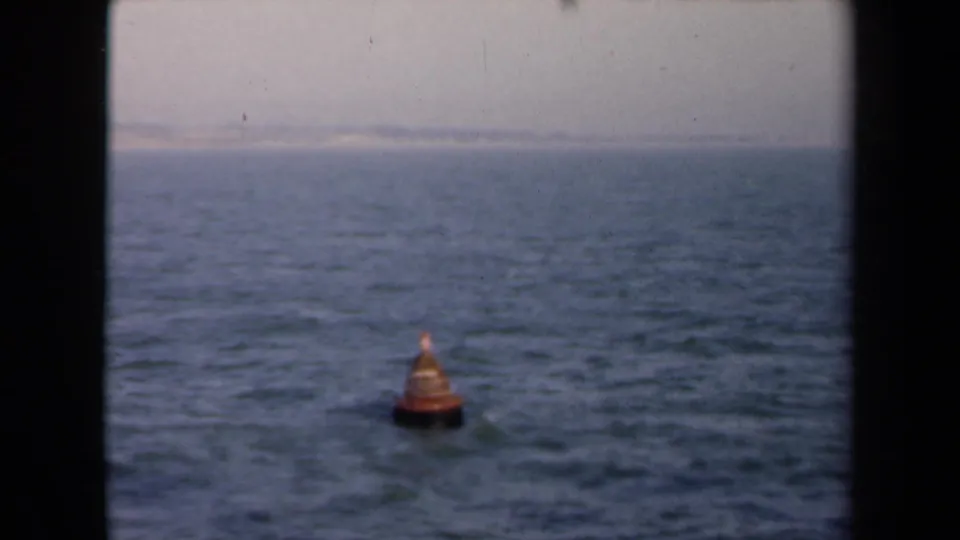 1946 Netherlands 8mm frame with an orange sea marker centered on rippled water, framed by dark vertical gate edges.