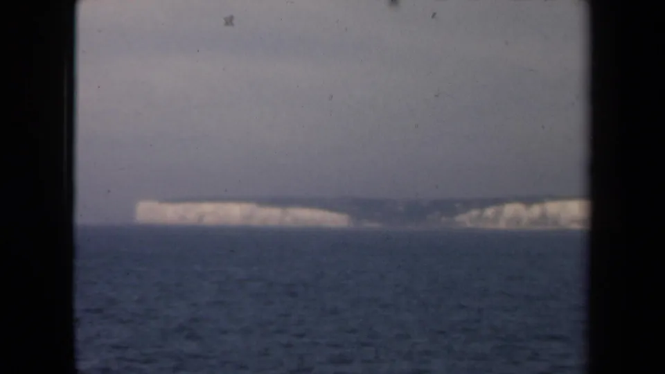 1946 Netherlands 8mm frame showing distant pale shoreline or cliffs beyond open water, with soft focus and visible film wear.