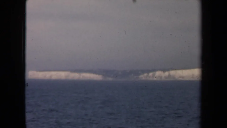 1946 Netherlands 8mm frame looking across open water toward a pale shoreline or cliff line under a gray-blue sky.