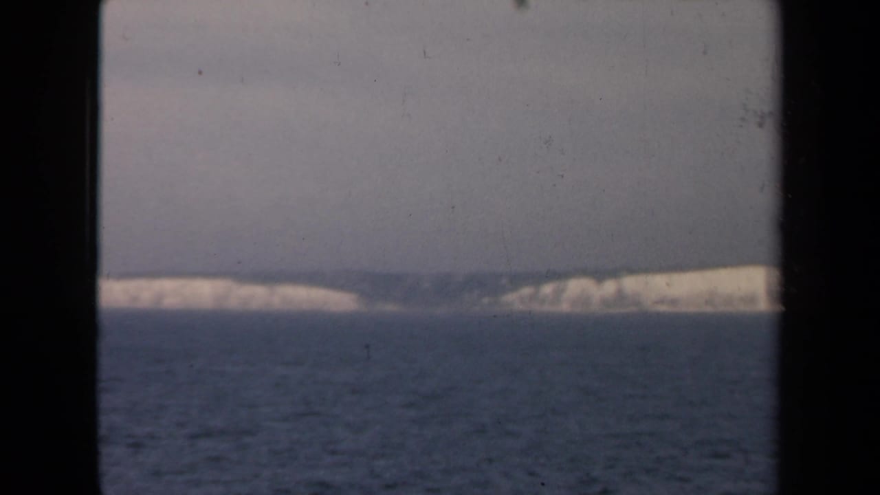 1946 8mm home-movie frame showing a hazy distant pale coastline across ocean, seen through dark vertical framing.