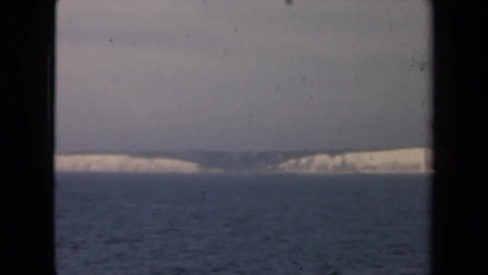 1946 8mm home-movie frame showing a hazy distant pale coastline across ocean, seen through dark vertical framing.