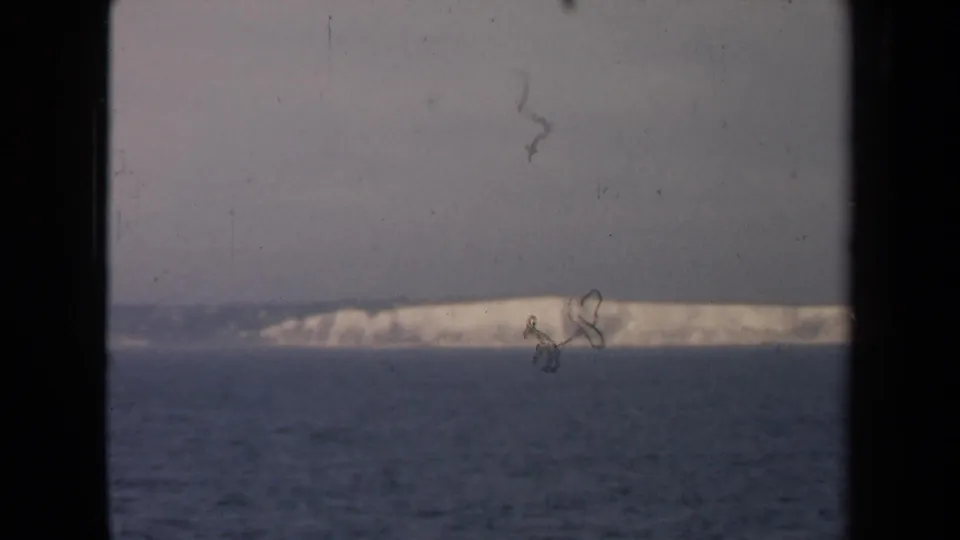 Archival 1946 8mm sea view showing a low pale coastline in haze, bordered by dark vertical framing.