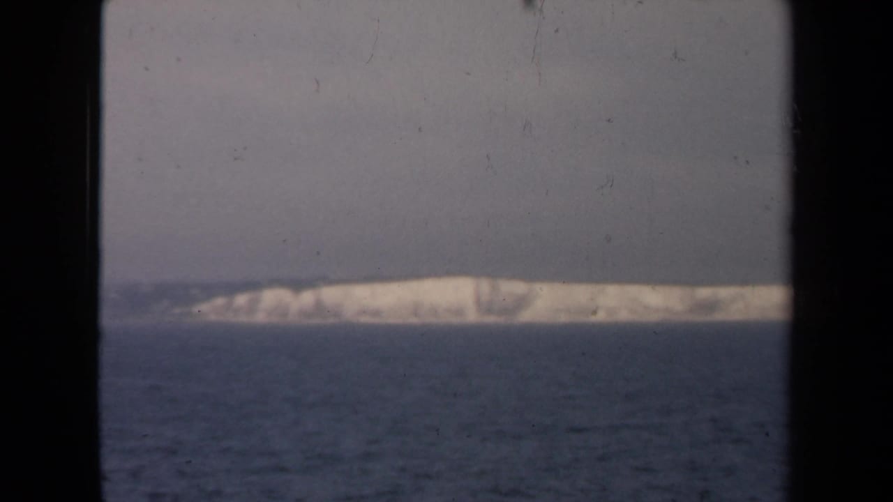 View across dark water toward a pale distant shoreline, framed by a train window.