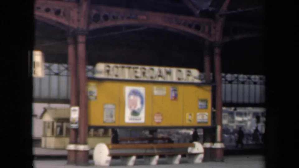 1946 Netherlands station view showing Rotterdam D.P. signage beneath an iron canopy with posters and a wooden bench.