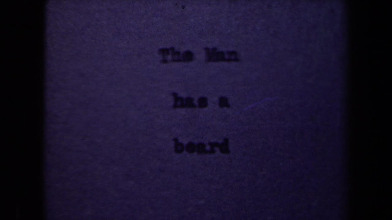 1940s 8mm frame showing a dim typed title card reading The Man has a beard, with heavy grain and dark vertical film borders.