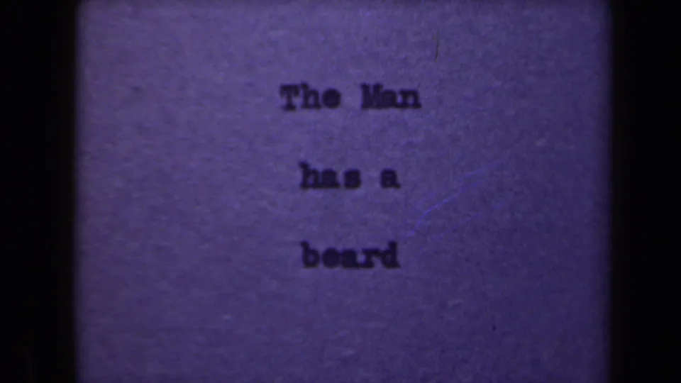 A repeated 8mm title-card frame shows the typed phrase The Man has a beard with visible grain, scratches, and uneven exposure.