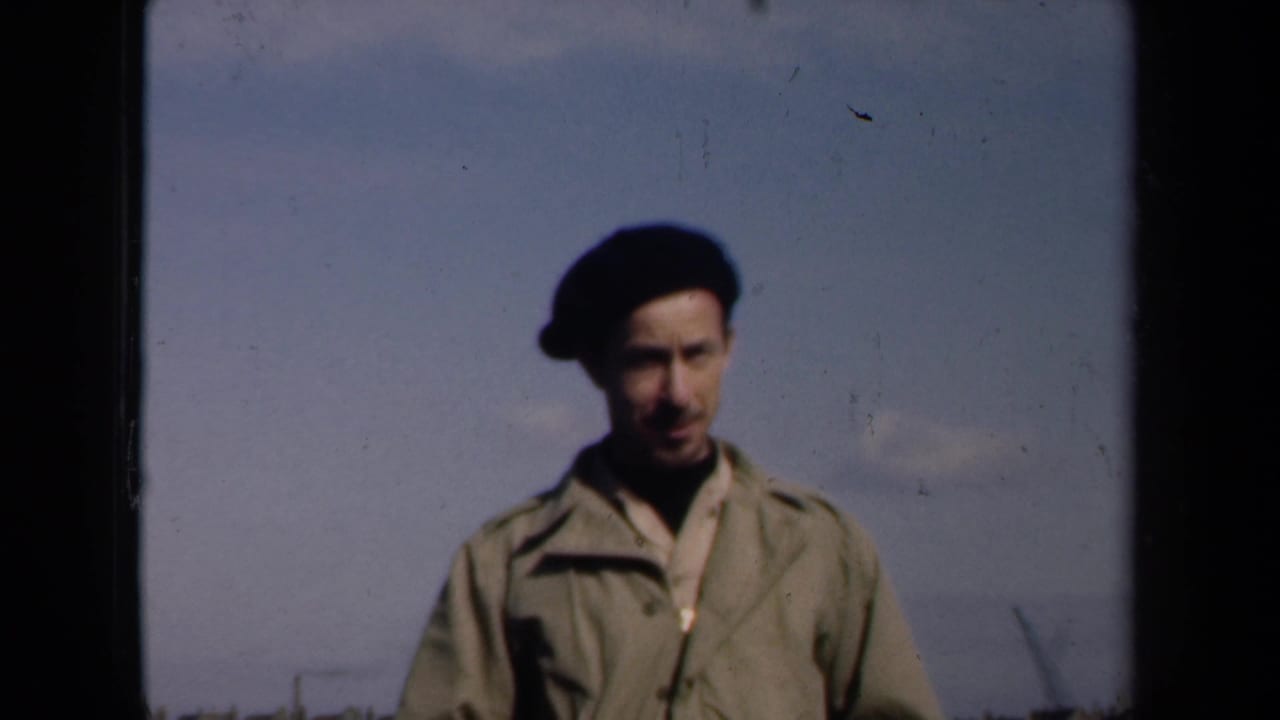 Man in a beret faces the camera against a mostly open sky on a rooftop.