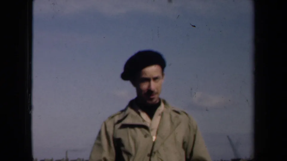 The man faces the camera in a black beret and light jacket, with an open rooftop skyline behind him in the Netherlands footage.