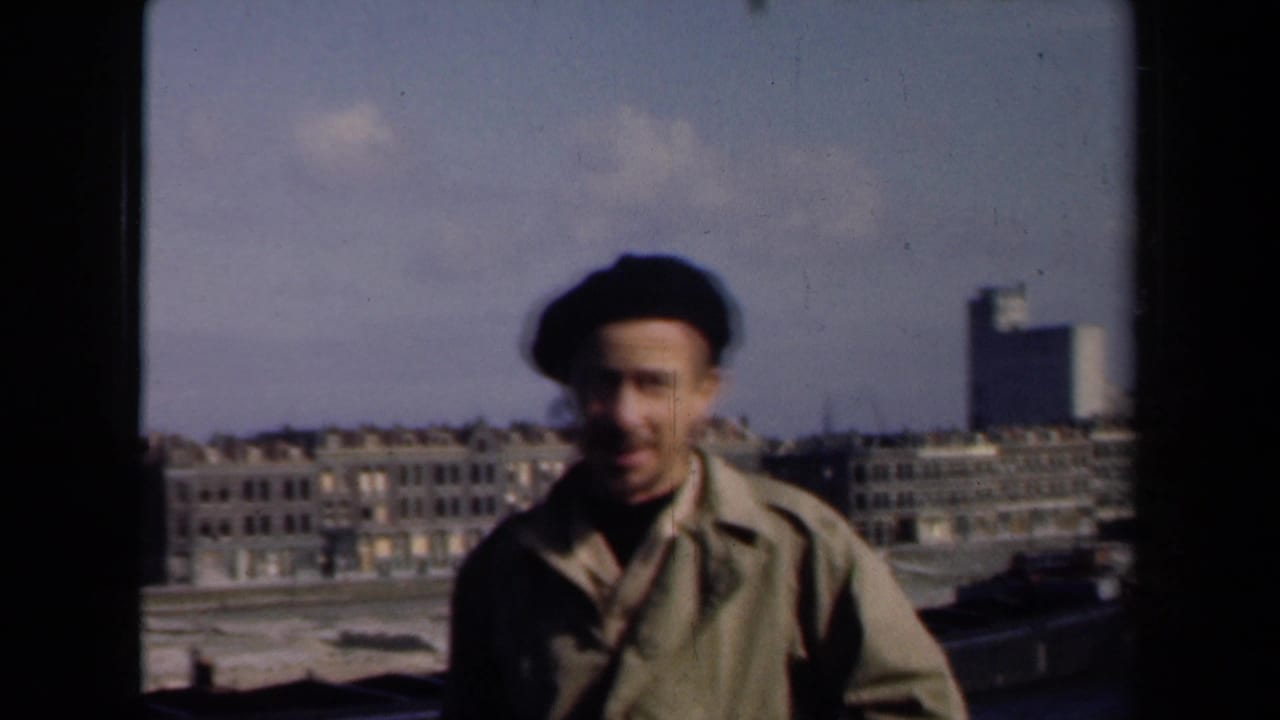 In 1946 Netherlands home-movie footage, an adult man in a dark beret faces the camera with city buildings and a high-rise behind him.