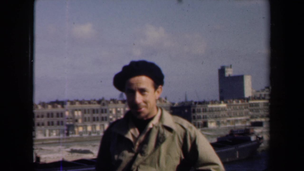 Man in beret framed against rows of buildings and a cloudy sky.