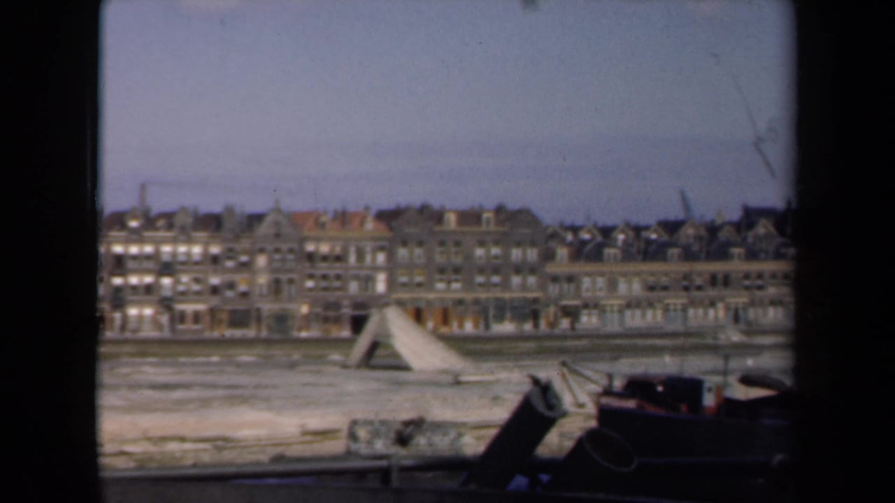 Row of waterfront buildings across water with a dark boat edge and wooden structure in front.