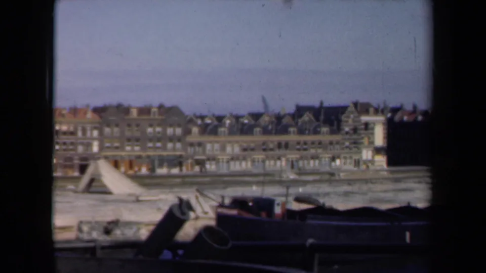 1946 Netherlands home-movie still of waterfront buildings under a pale sky, with a dark vessel and film border in the foreground.
