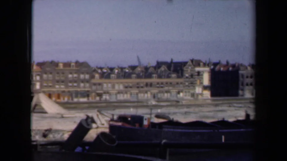 1946 Netherlands home-movie view of waterfront buildings, gabled roofs, muddy shore, and dark barges in the foreground.