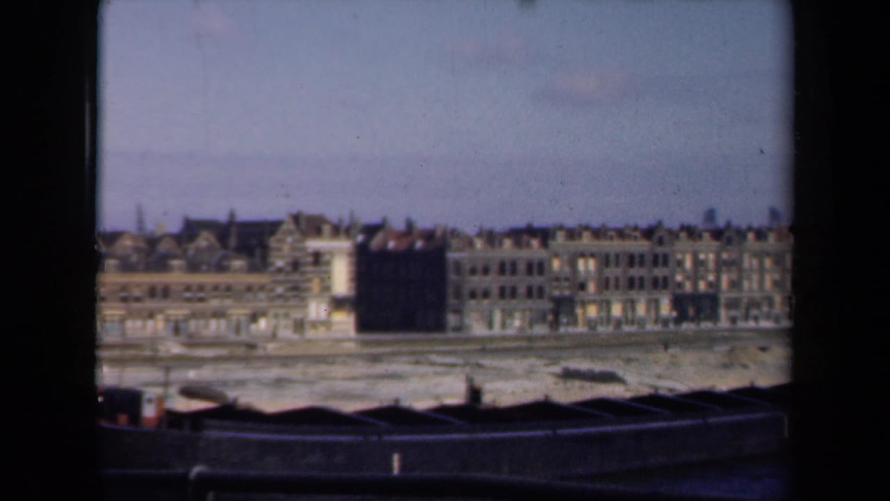 1946 Netherlands 8mm view of damaged waterfront buildings across a pale shoreline from a high, distant vantage point.